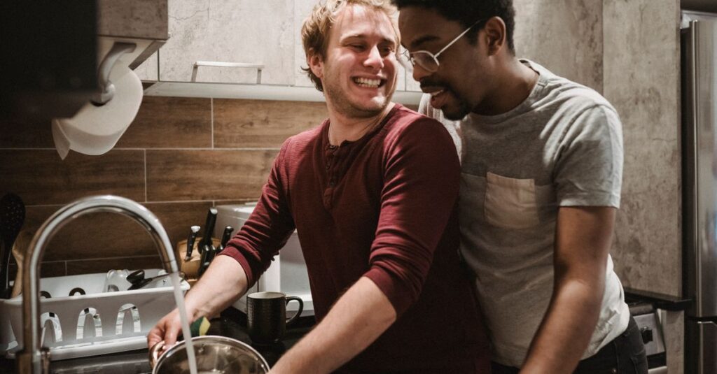 夫婦が家事の役割を交換し、夫が料理・妻が掃除をしている様子。笑顔で協力しているシーン。