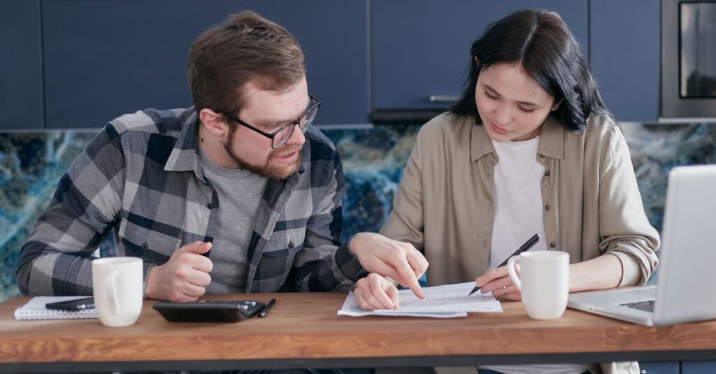 夫婦がノートPCで家事分担表をスプレッドシートにまとめている様子。分担比率を話し合うシーン。